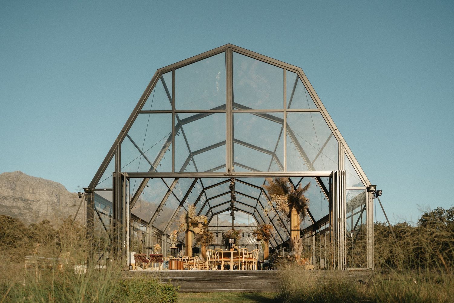 A rustic greenhouse frame with metal beams sits in a desert landscape against a teal-tinted sky.