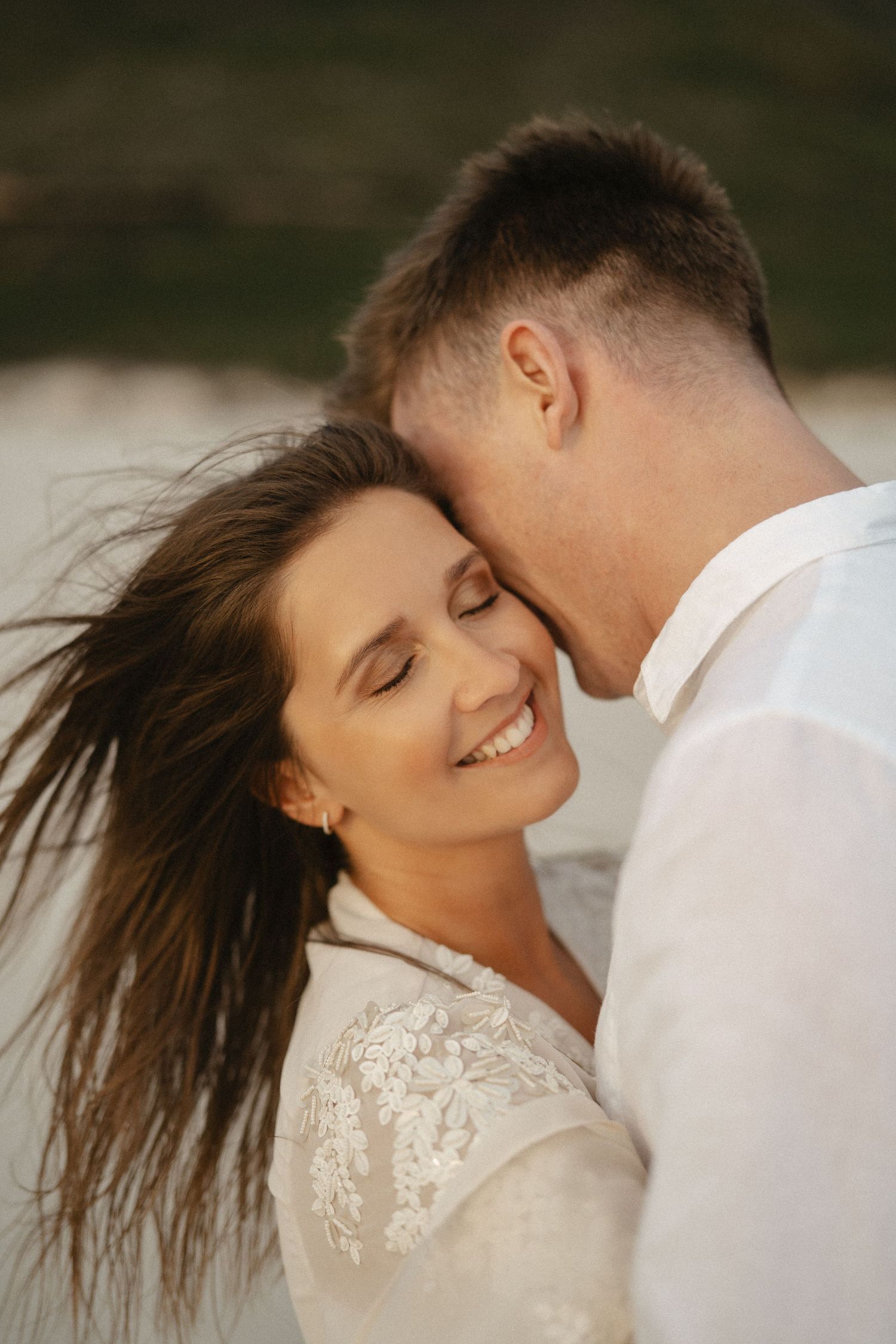 Romantic couple embracing outdoors with wind blowing through long dark hair as they share an intimate moment together.