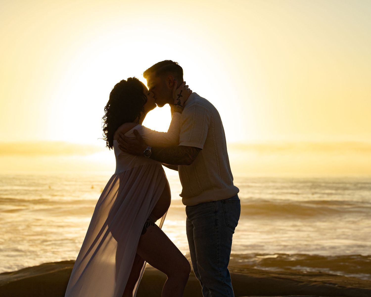 A romantic silhouette of a couple embracing at sunset on the beach with golden light and ocean waves in the background.