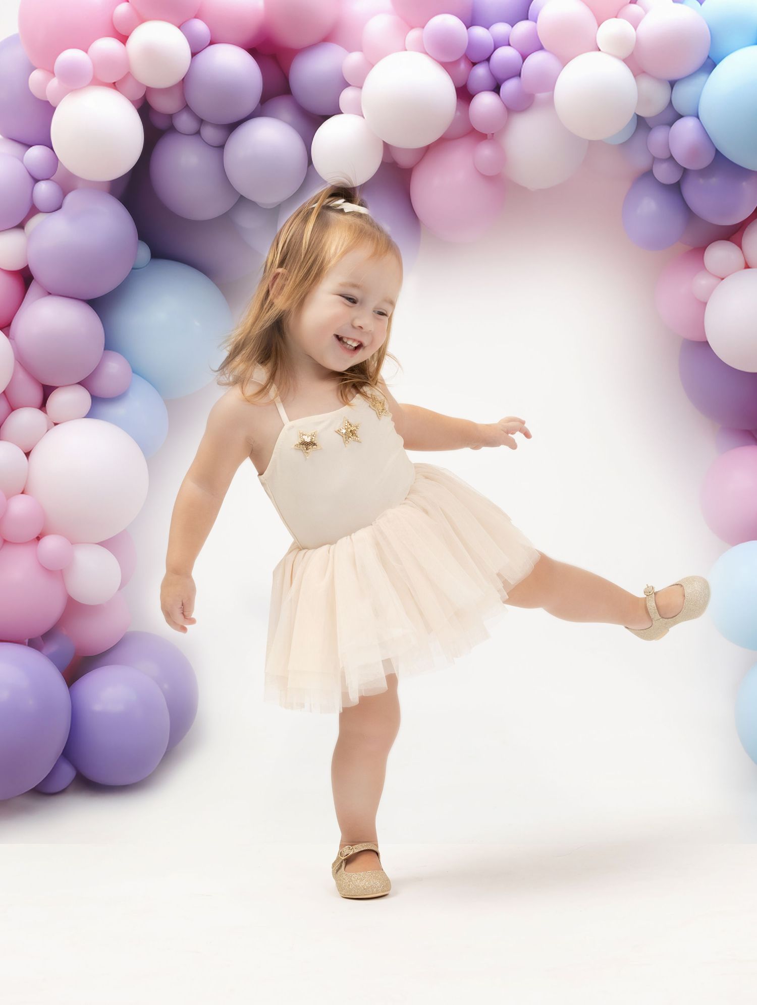 White tulle dress with gold stars against a pastel balloon arch backdrop in a dreamy portrait setting.