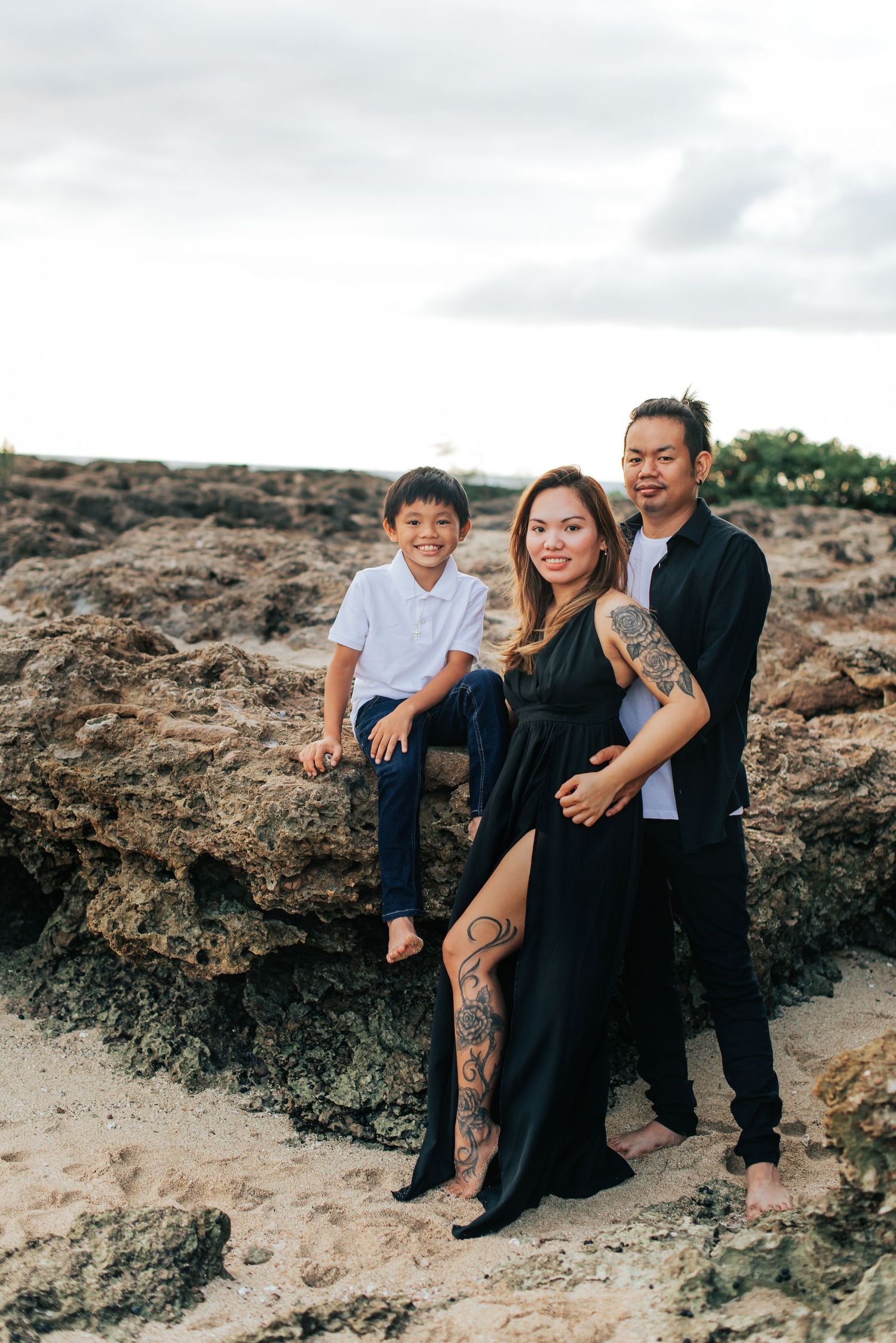 A family in black outfits poses together on rocky coastal terrain at sunset.