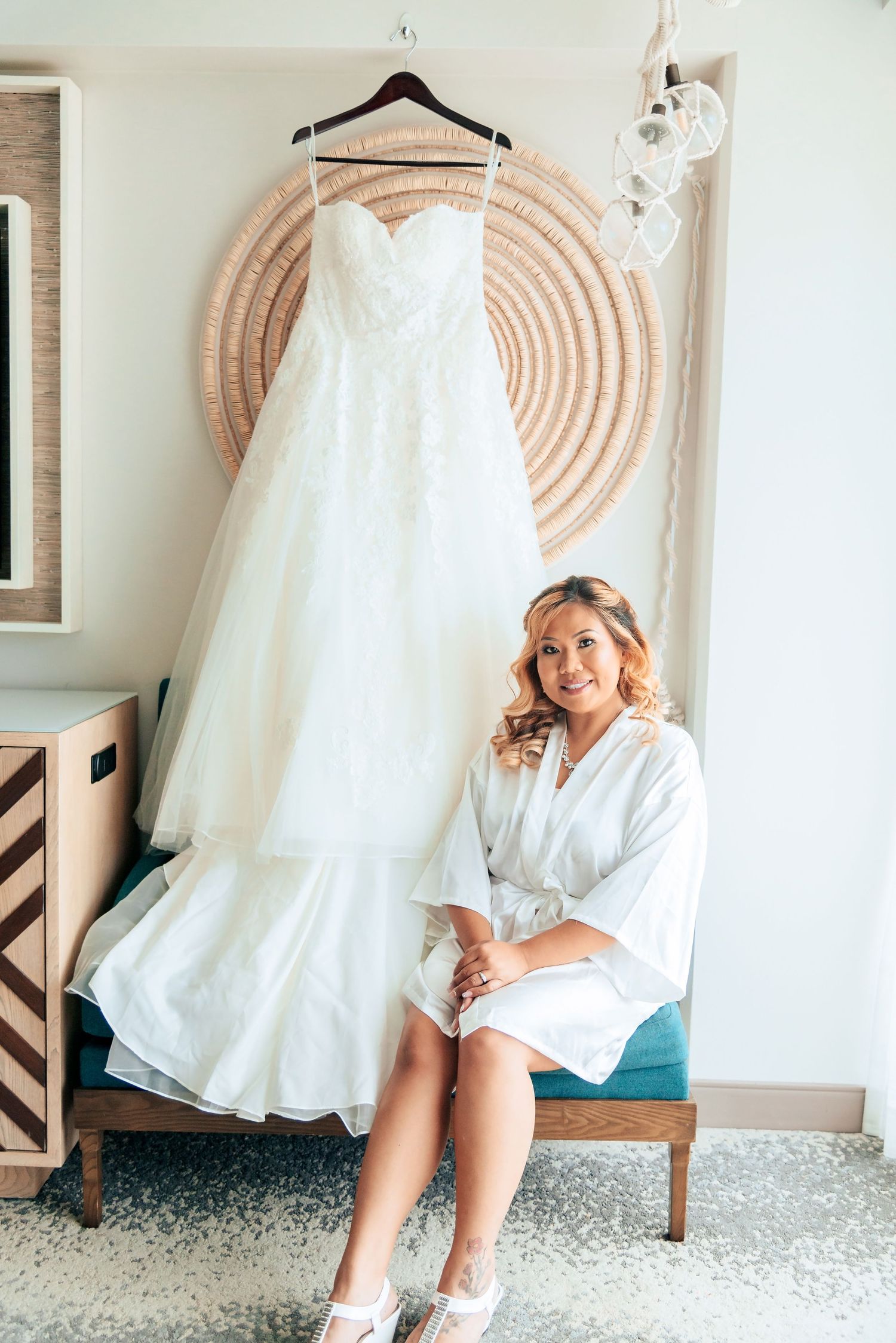 A white wedding dress hangs on display above a decorated room with circular wall art and modern furniture.
