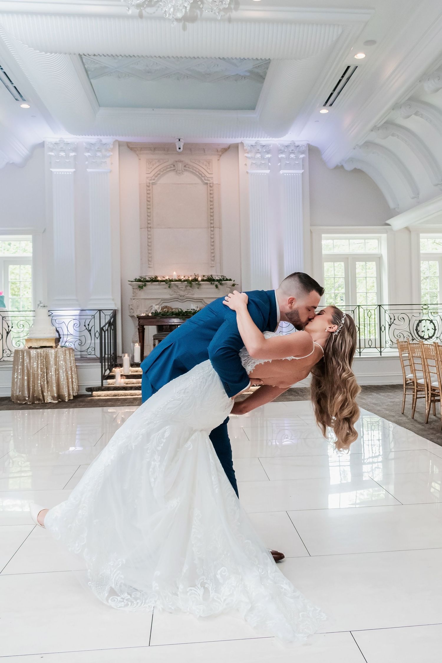 Romantic dip pose on a bright ballroom floor with elegant white and gold decor in a luxurious venue.