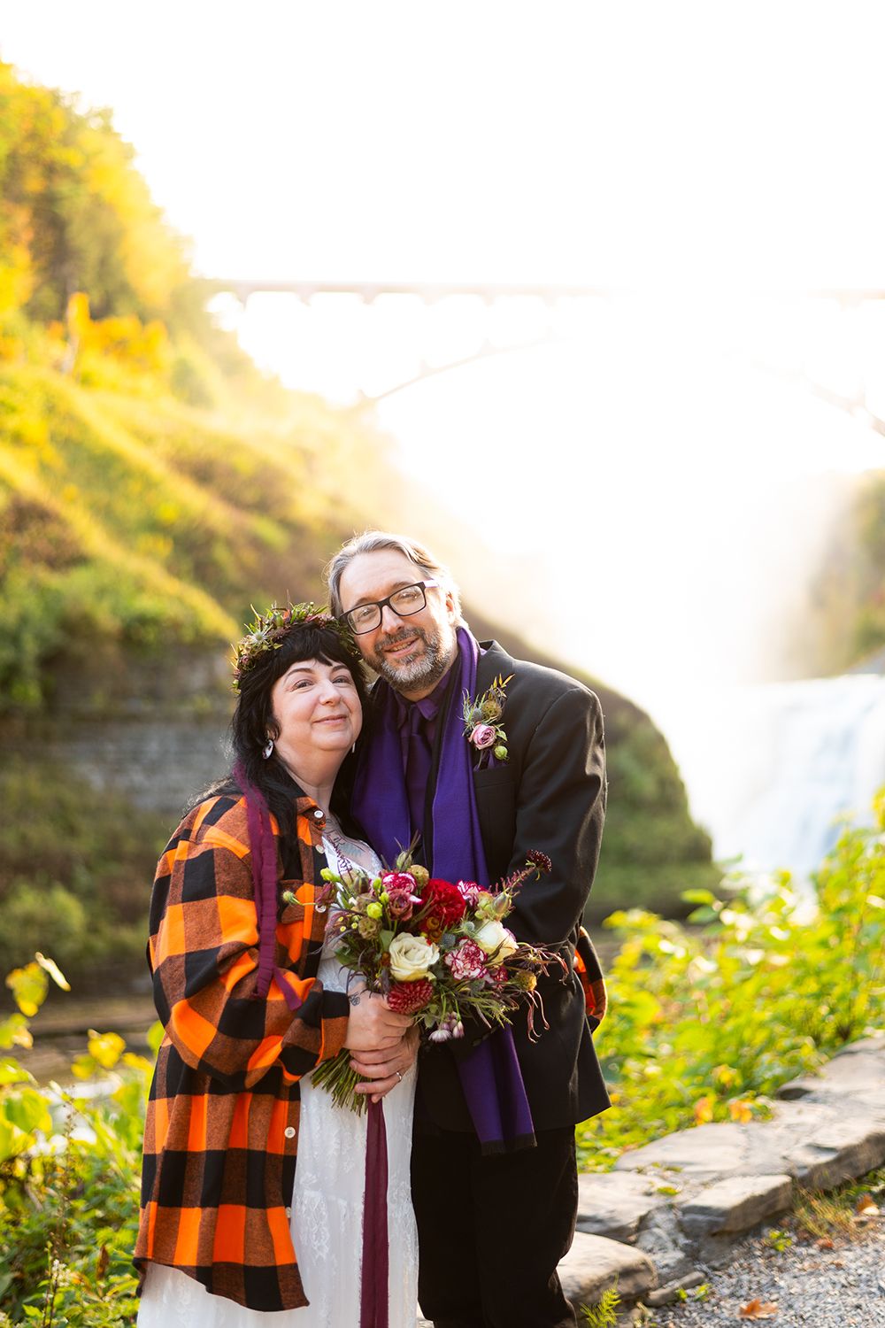 A couple poses together with a bouquet against a scenic autumn waterfall backdrop at Letchworth State Park.