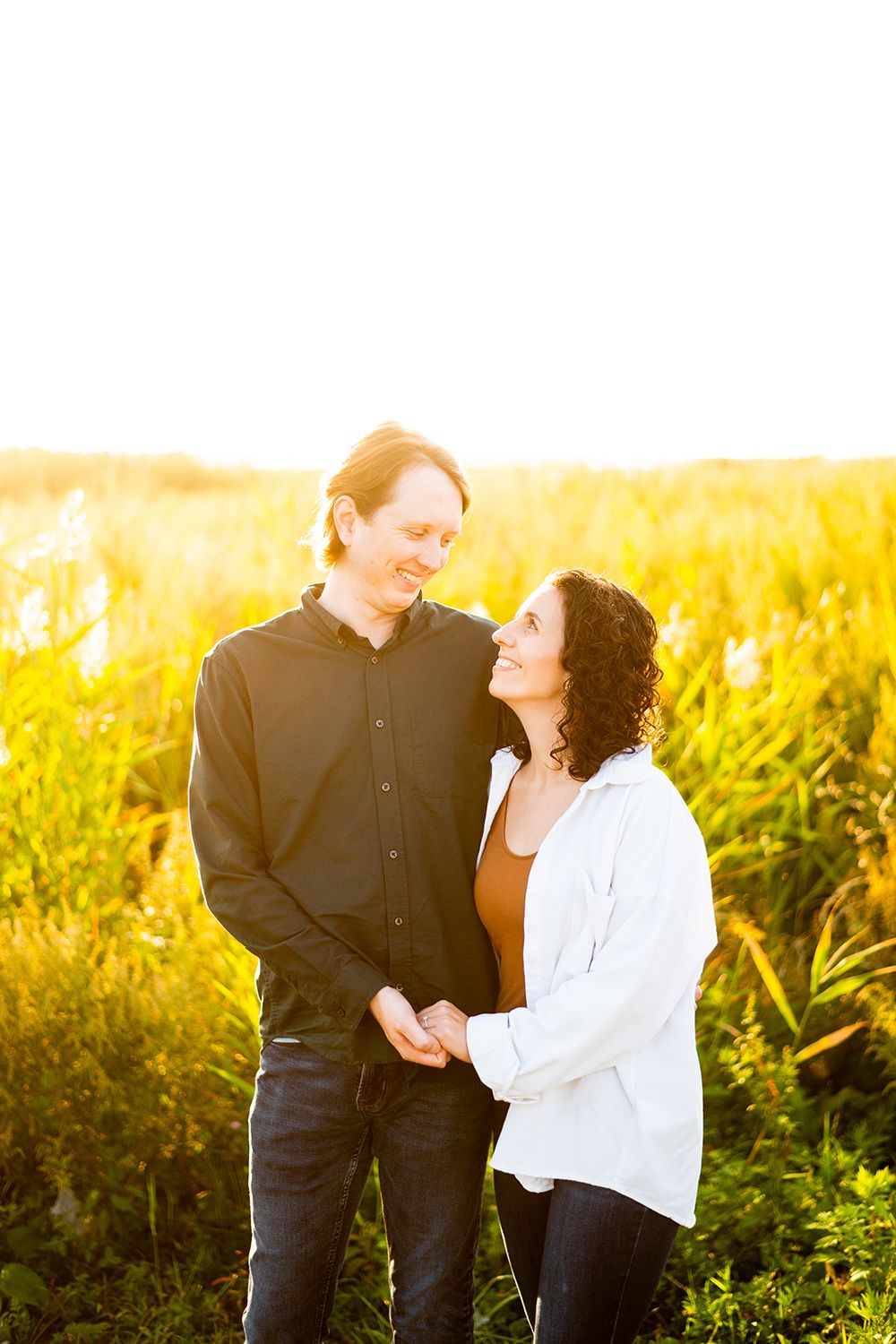 Couple sharing a romantic sunset moment in a golden field with tall grasses and warm sunlight.