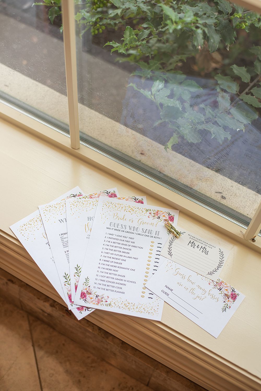 Wedding invitation cards with floral designs and text arranged on a windowsill with natural light coming through.