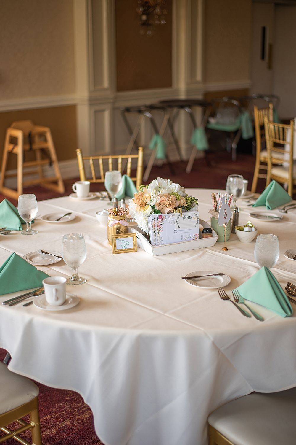 Elegant wedding reception tables set with crisp white linens, mint green napkins, and delicate centerpieces in a banquet hall.