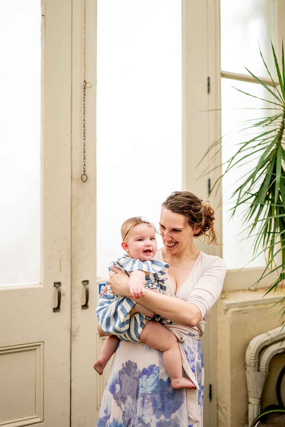 Joyful candid moments captured in a bright sunroom with potted plants and white French doors.
