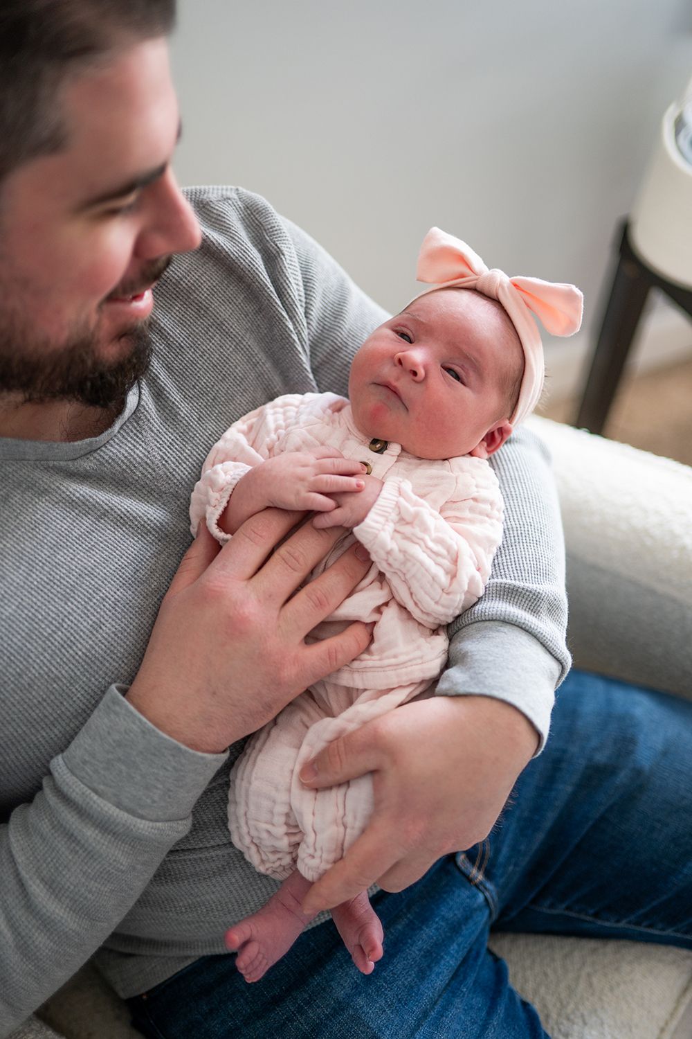 Parent in gray sweater holds and comforts small baby in pink outfit while sitting on couch in candid photo series.