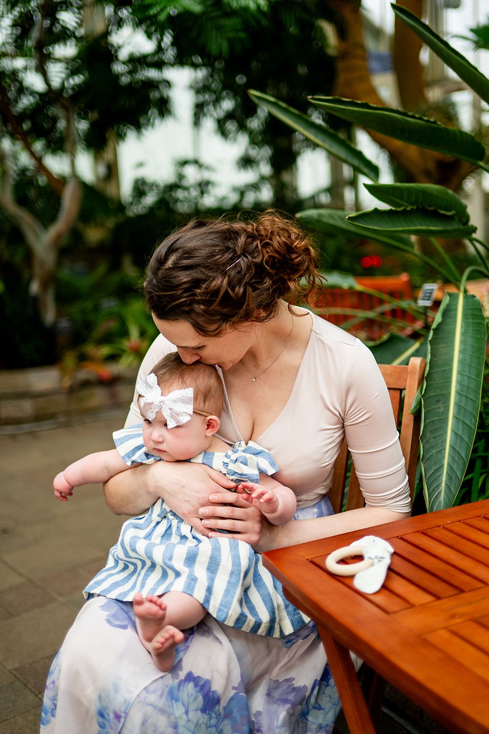A tender moment shared between parent and infant sitting together on a wooden bench among green foliage.