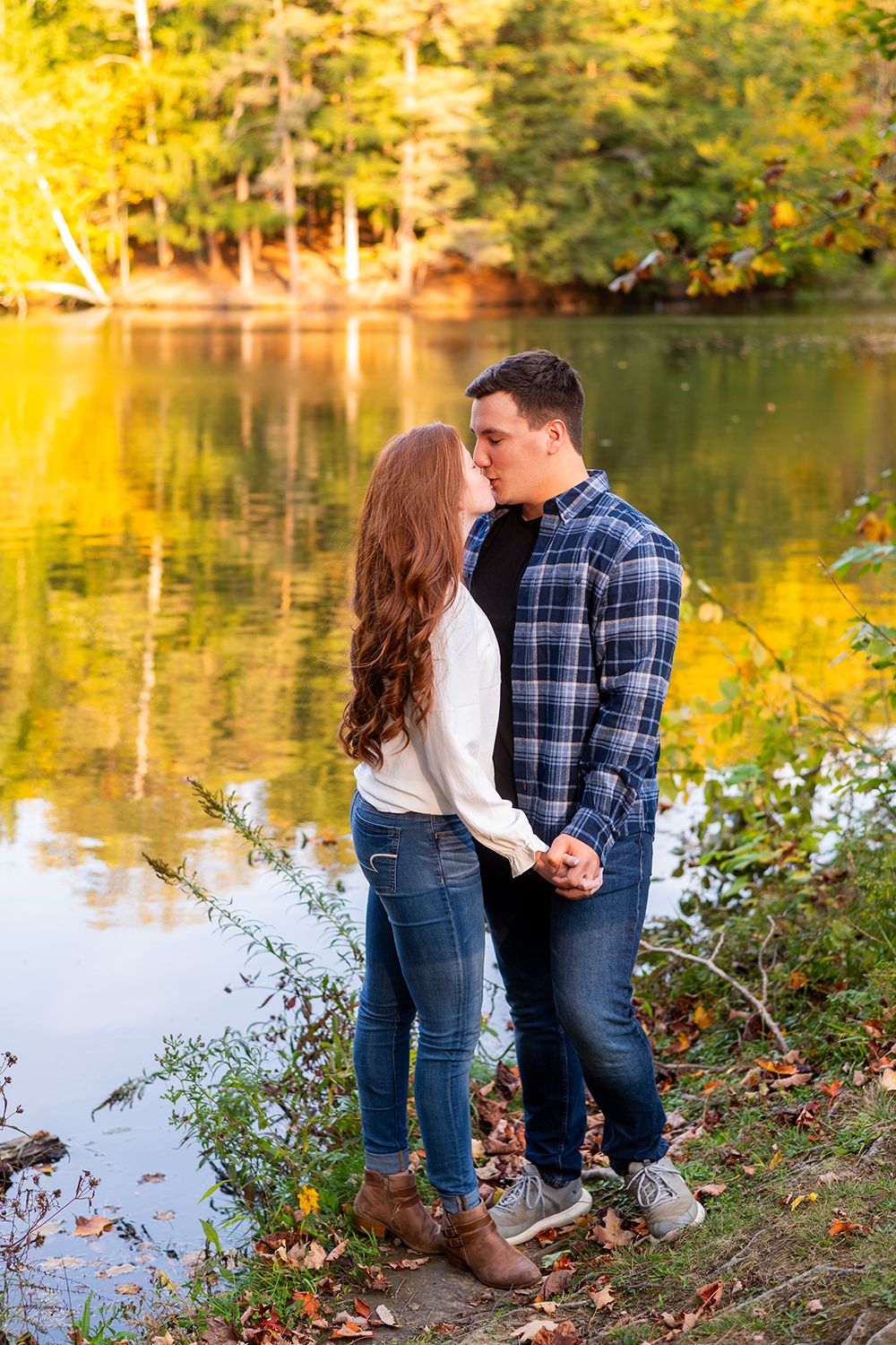 A couple shares a tender moment by a tranquil lake surrounded by autumn foliage and golden light.