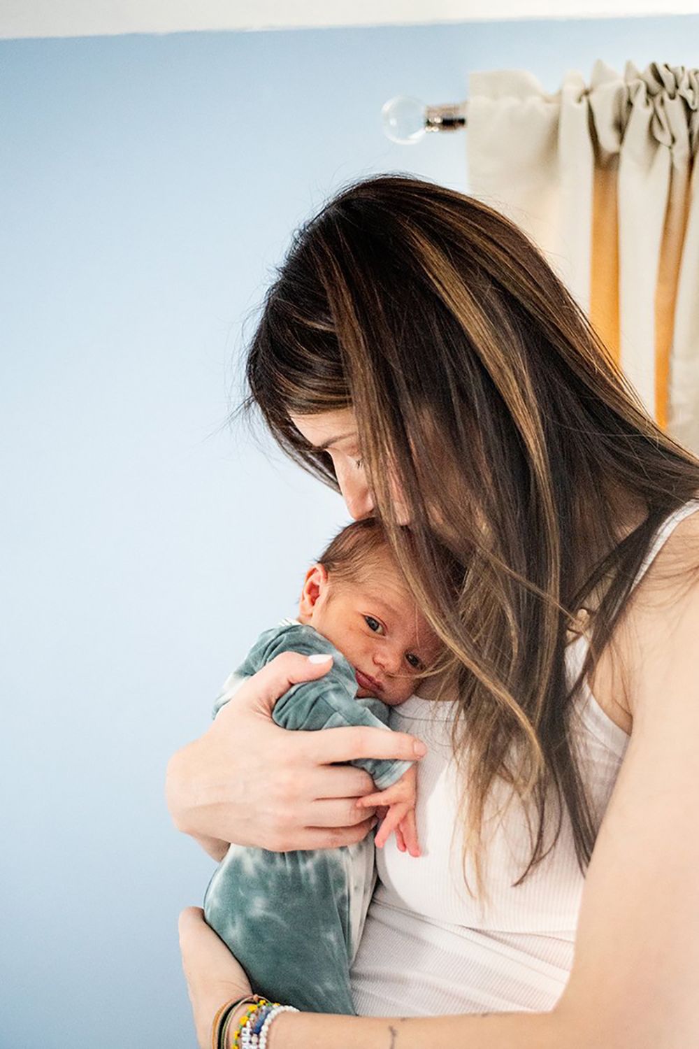 A tender moment captured as a parent in a white tank top gently cradles a sleeping baby in turquoise clothing.