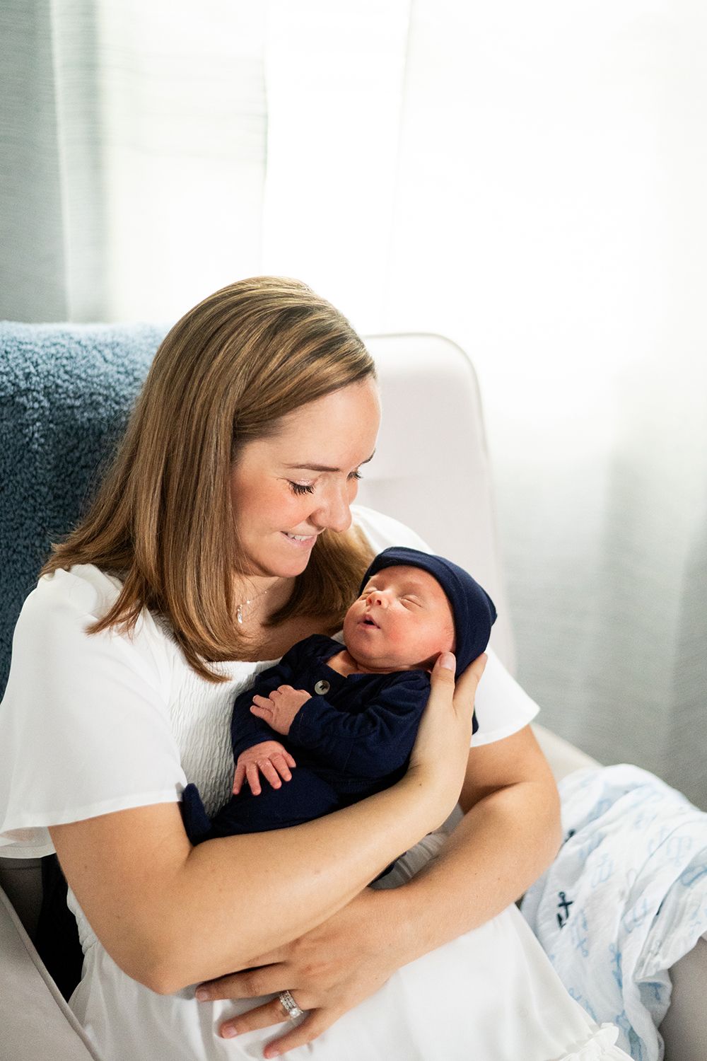 A tender moment between parent and newborn baby in white and navy blue clothing beside a window.