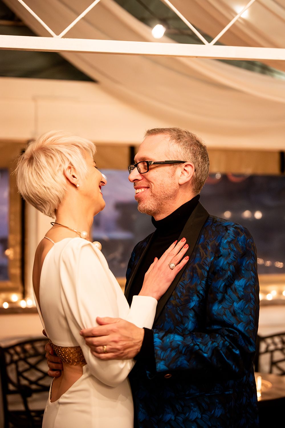 A couple shares an intimate moment at an elegant indoor celebration with ambient lighting.