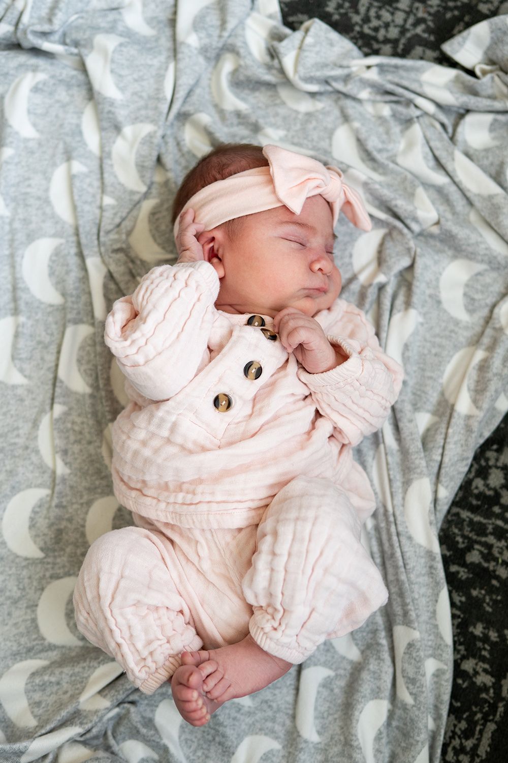 Newborn baby wearing soft pink knitted outfit lies peacefully on gray patterned blanket in series of photos.
