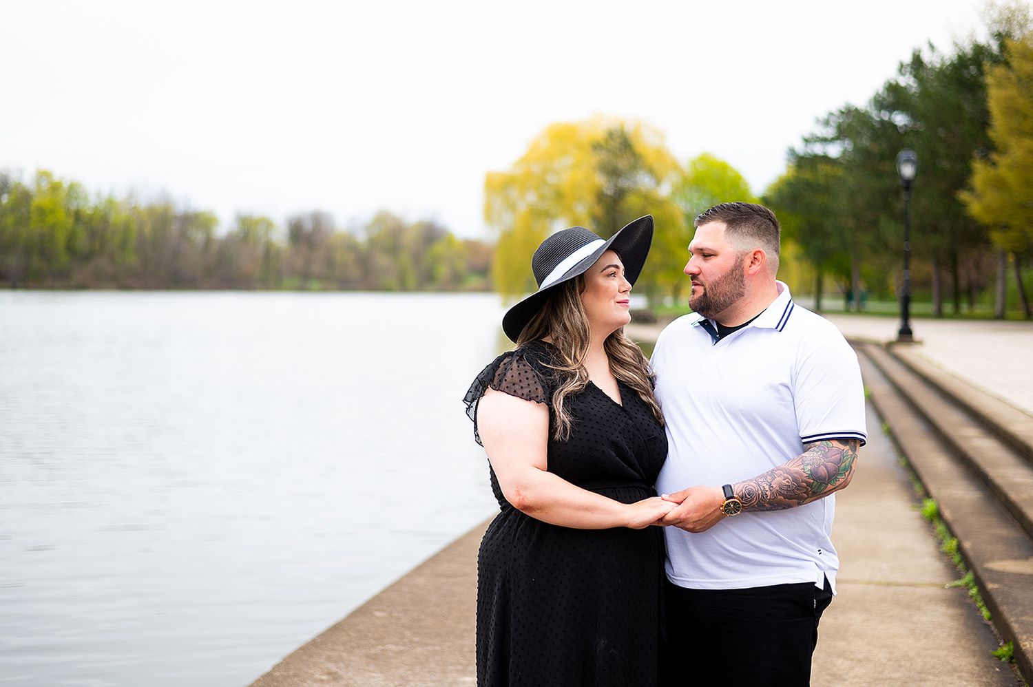 A couple shares a tender moment while walking along a lakeside path on a sunny spring day.