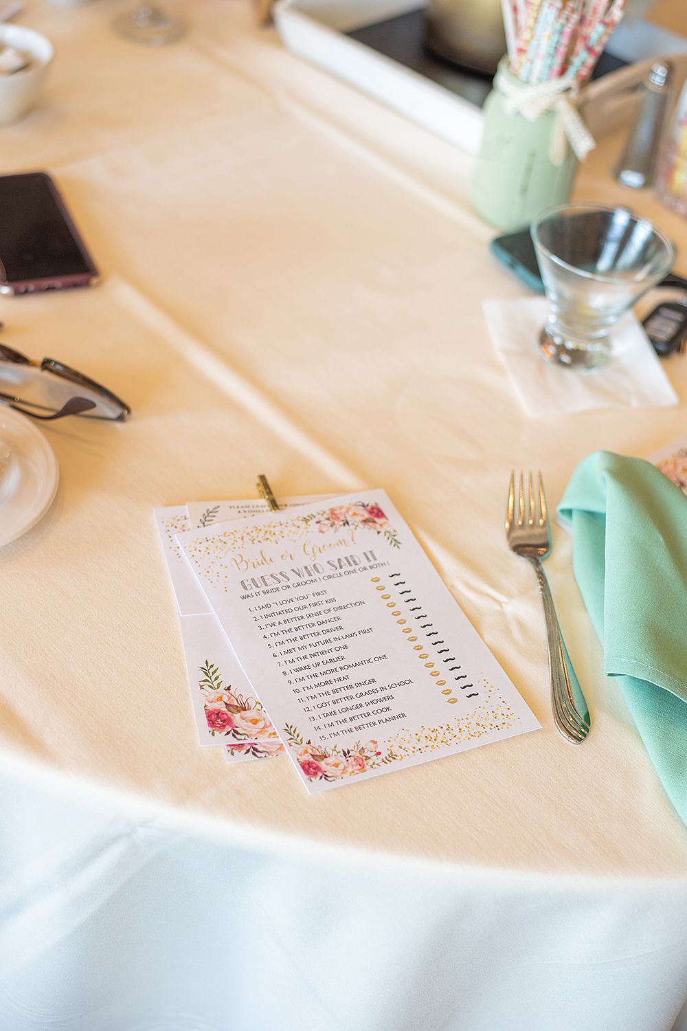 Wedding table setting with a floral menu card, mint napkin, and silverware on white tablecloth.