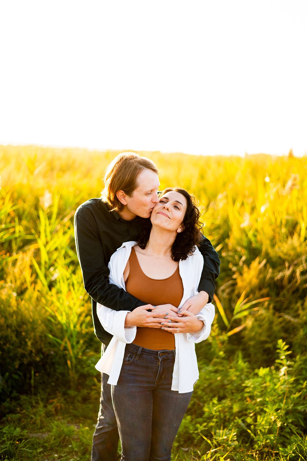 A romantic moment shared between a couple embracing in a sunlit field of golden grass at sunset.