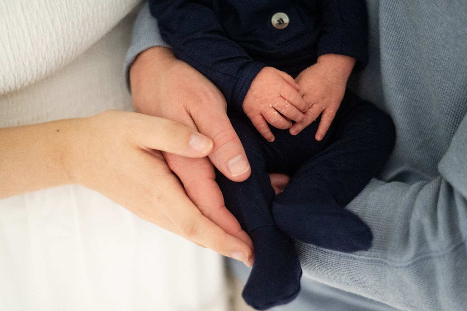 Close-up of tiny newborn feet in navy blue socks being gently held by caring hands.