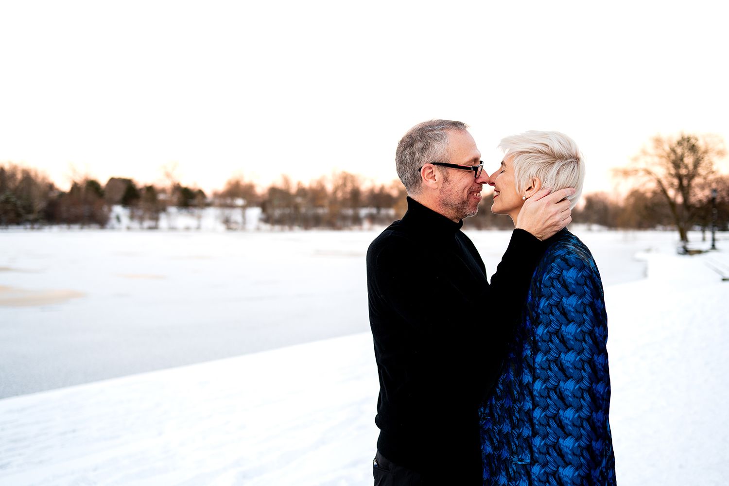 Intimate moment shared between two people in winter coats against a snow-covered backdrop.