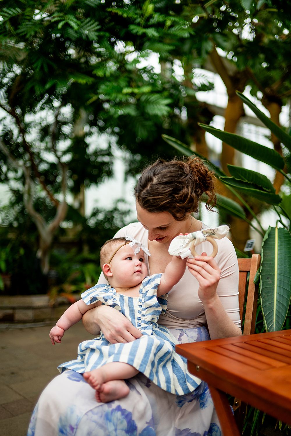 Mother and baby share tender moments while sitting in a lush greenhouse garden setting.
