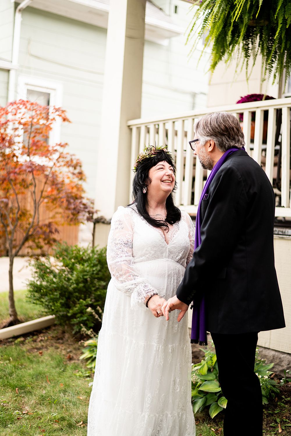 Joyful wedding couple share a candid moment together on a porch with autumn foliage in the background.