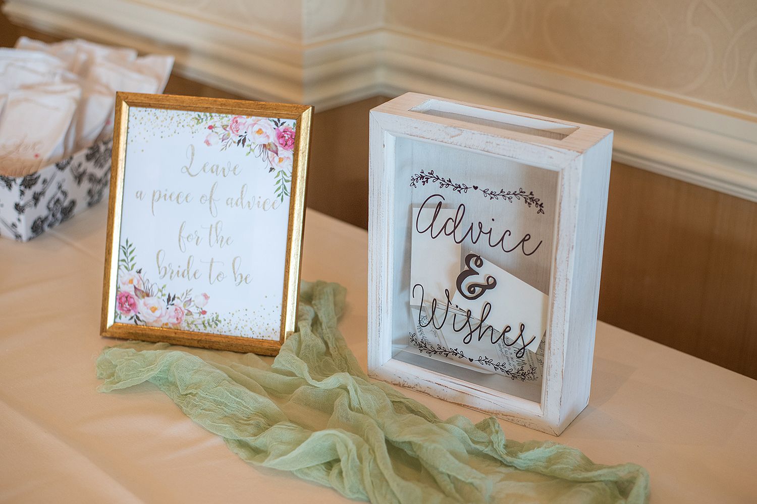 Wedding reception decor featuring two framed signs with floral accents and soft mint green tulle on a tablecloth.