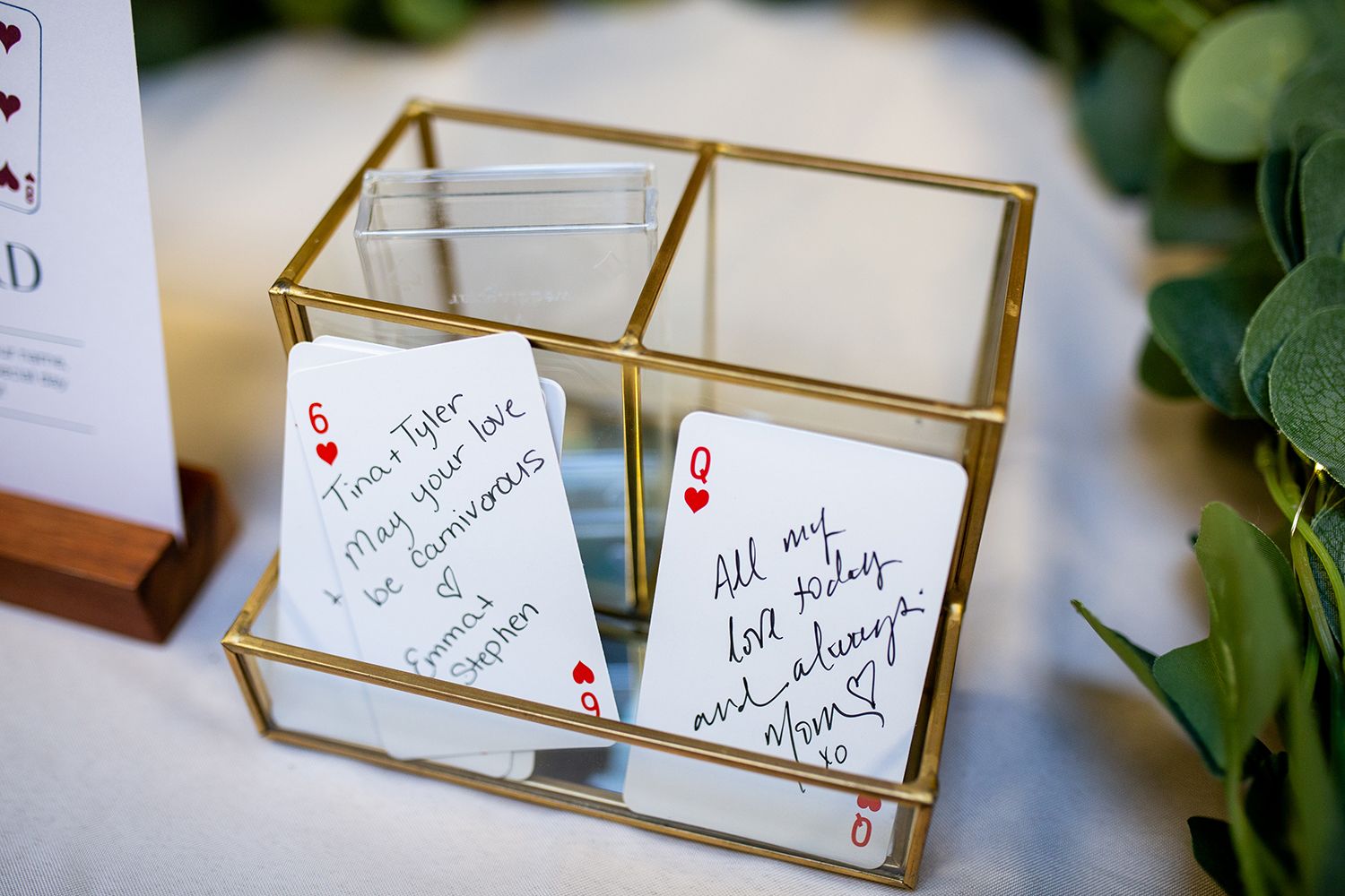 Playing cards displayed in a gold and glass box serving as unique wedding guest messages.