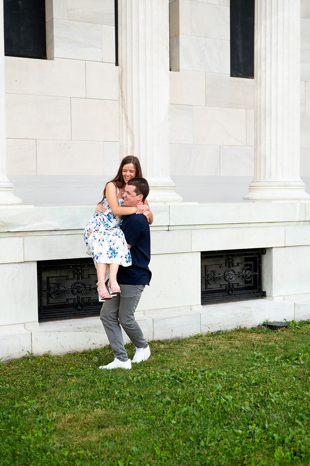 A sweet moment shared between a couple in front of white columns on a grassy lawn.