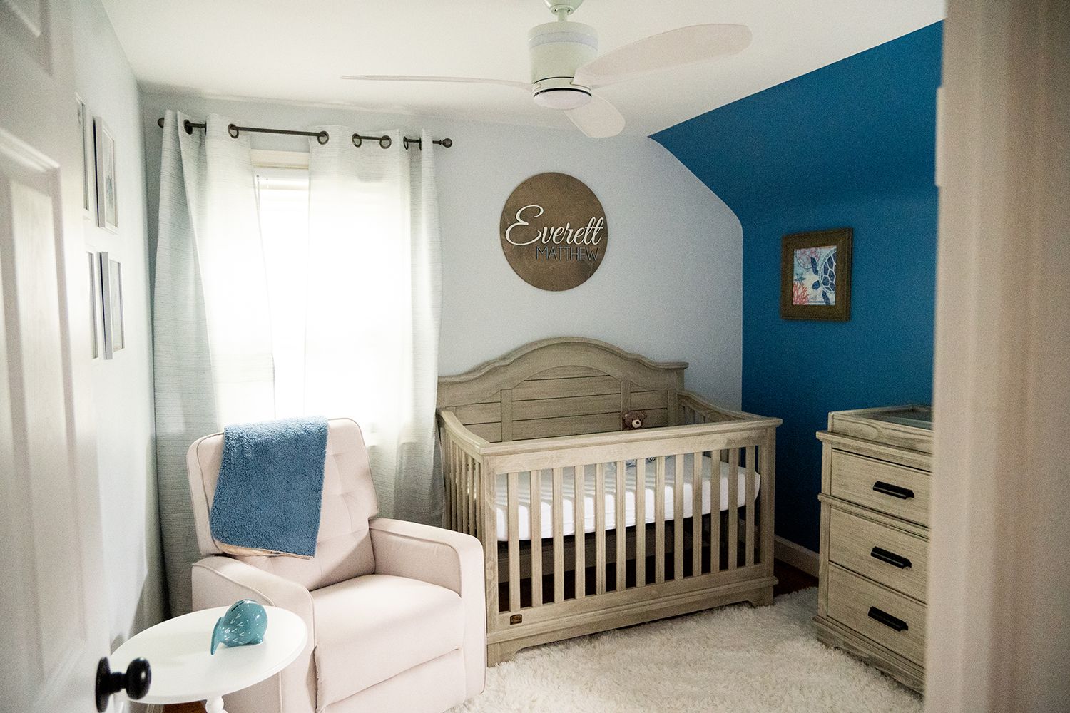 Modern blue and white nursery featuring a wooden crib, white glider chair, and name decoration on wall.