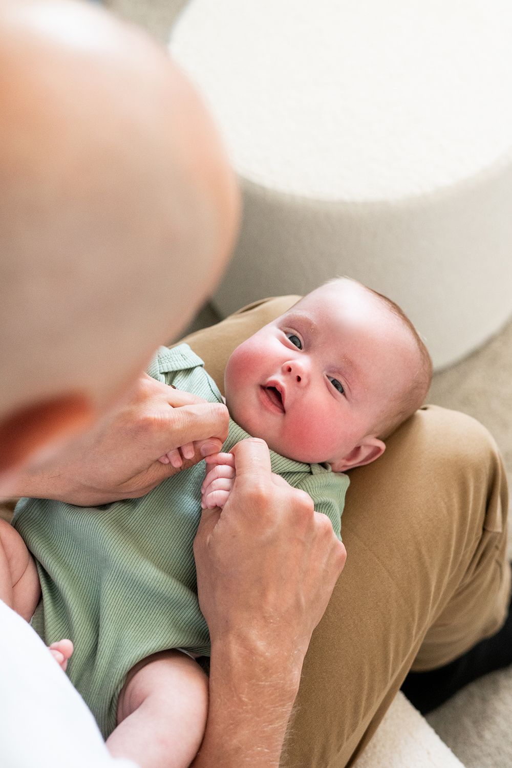 Baby in mint green onesie lying on lap with hands reaching down for care and attention.
