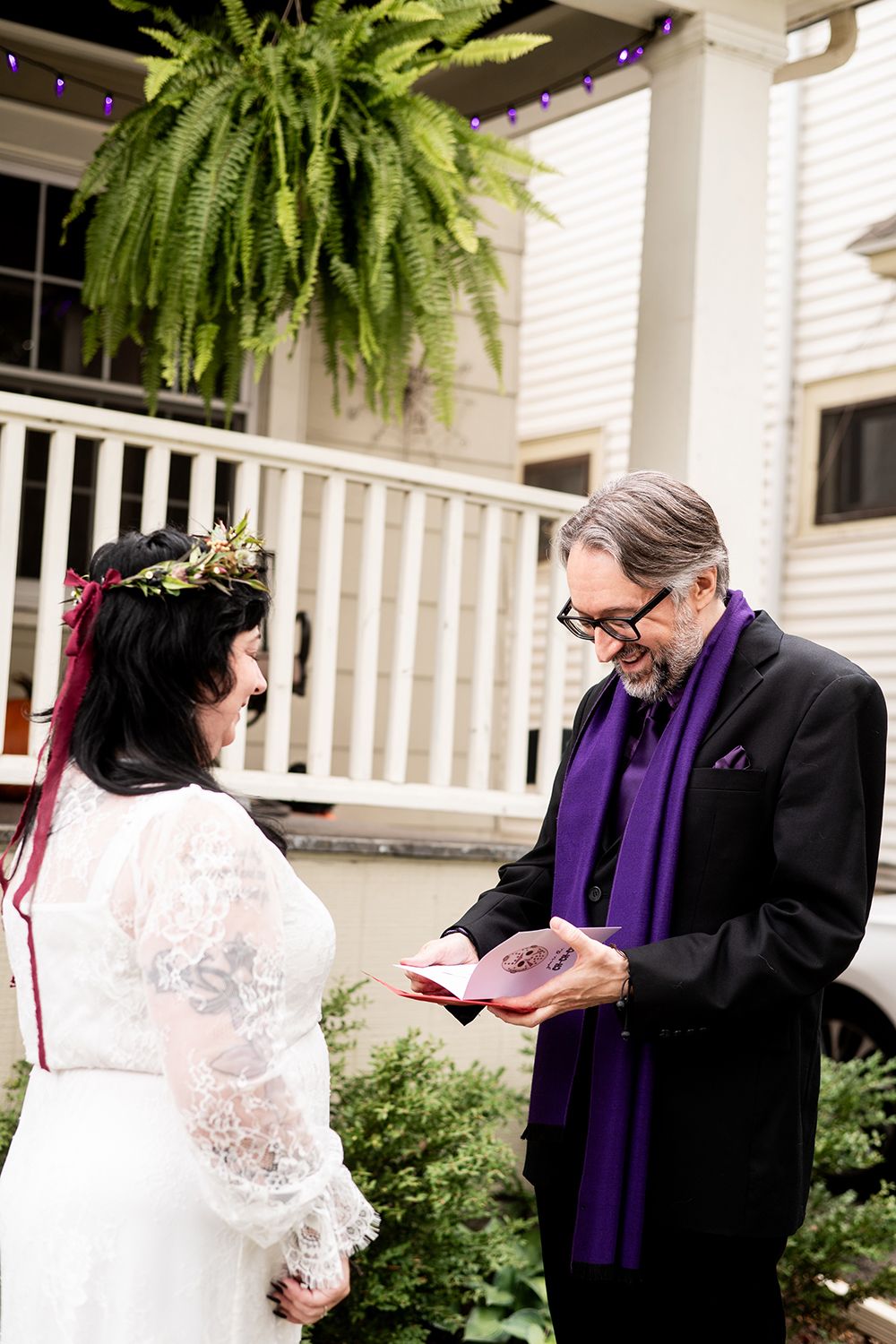 Wedding ceremony candid shot on a white-railed porch with hanging ferns and greenery.