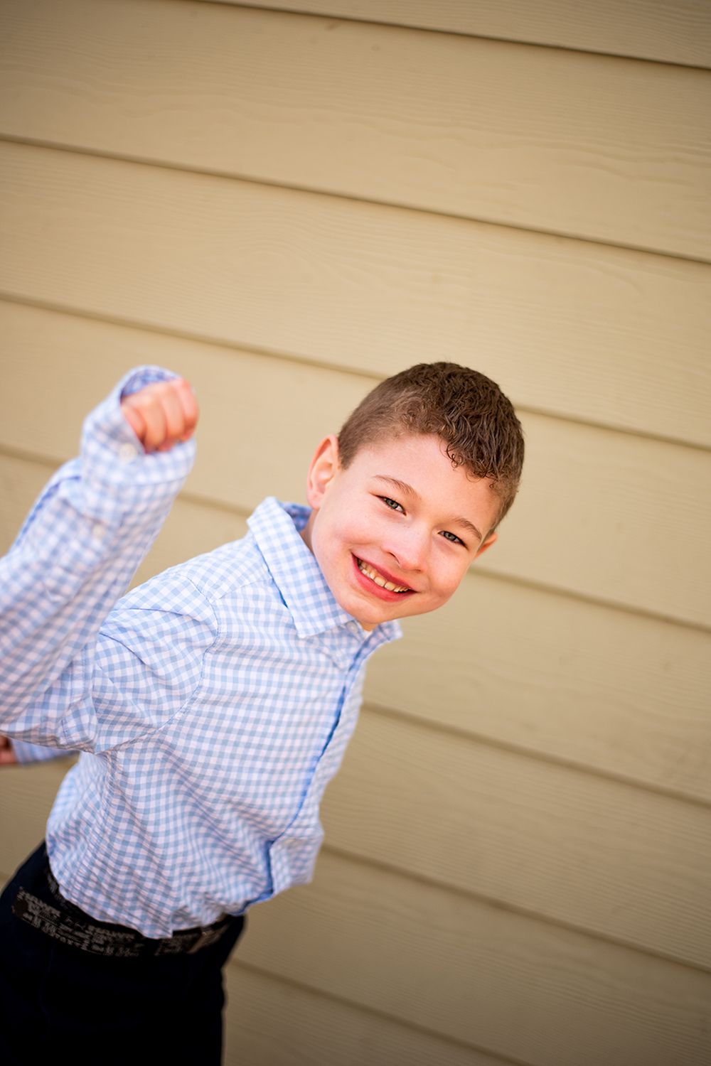 Playful portrait of young person in blue checkered shirt against beige wall.