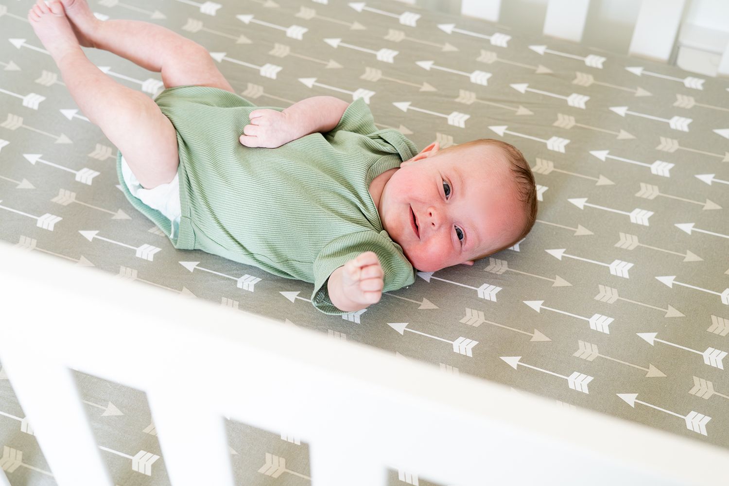 A smiling baby wearing a mint green onesie lies on a gray and white star-patterned crib sheet.