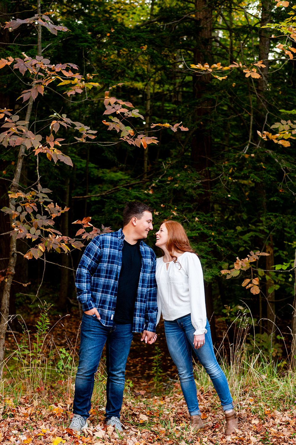 A couple shares a tender moment among autumn leaves and trees in a woodland setting.