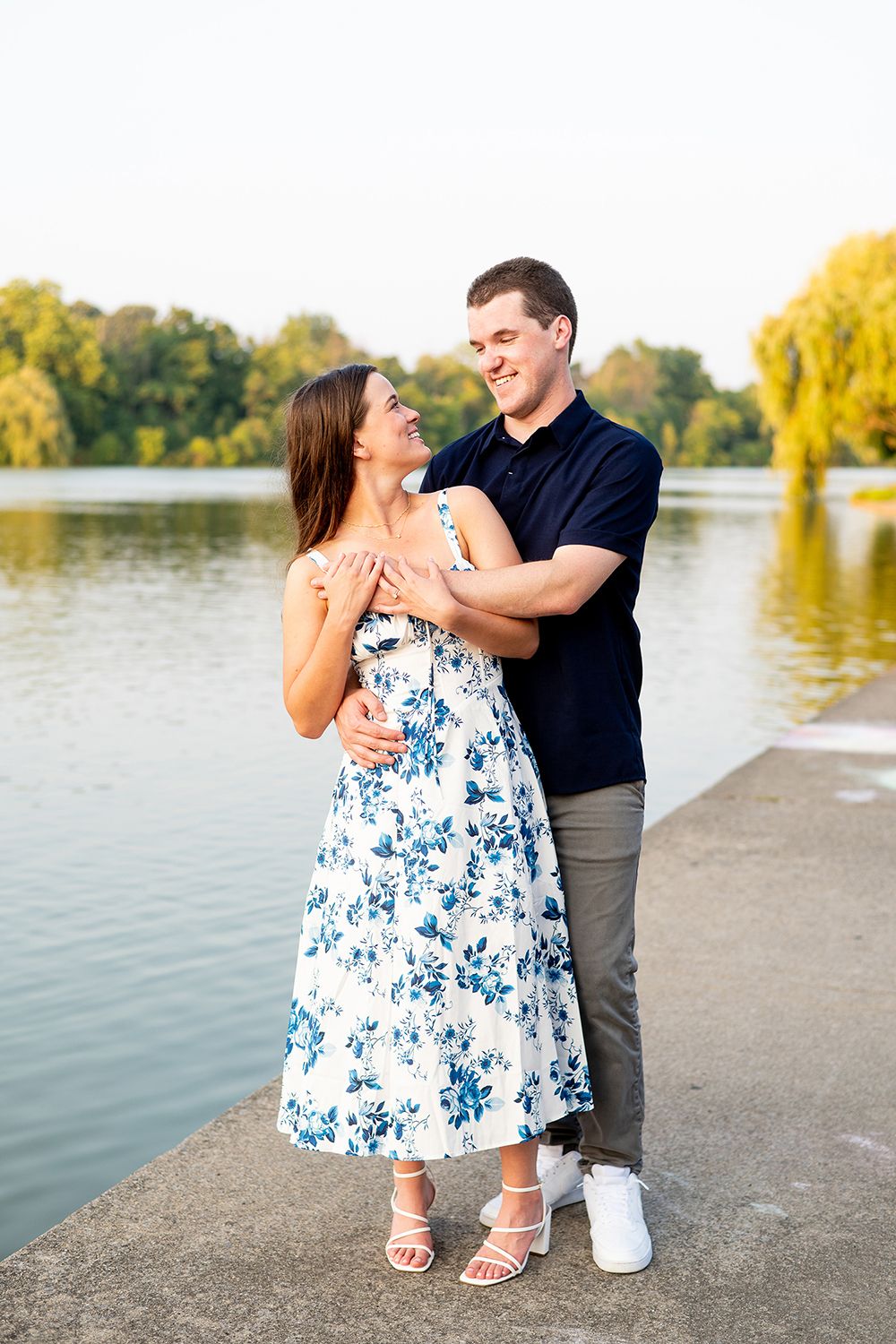 A romantic couple shares intimate moments while posing by a serene lakeside at sunset.