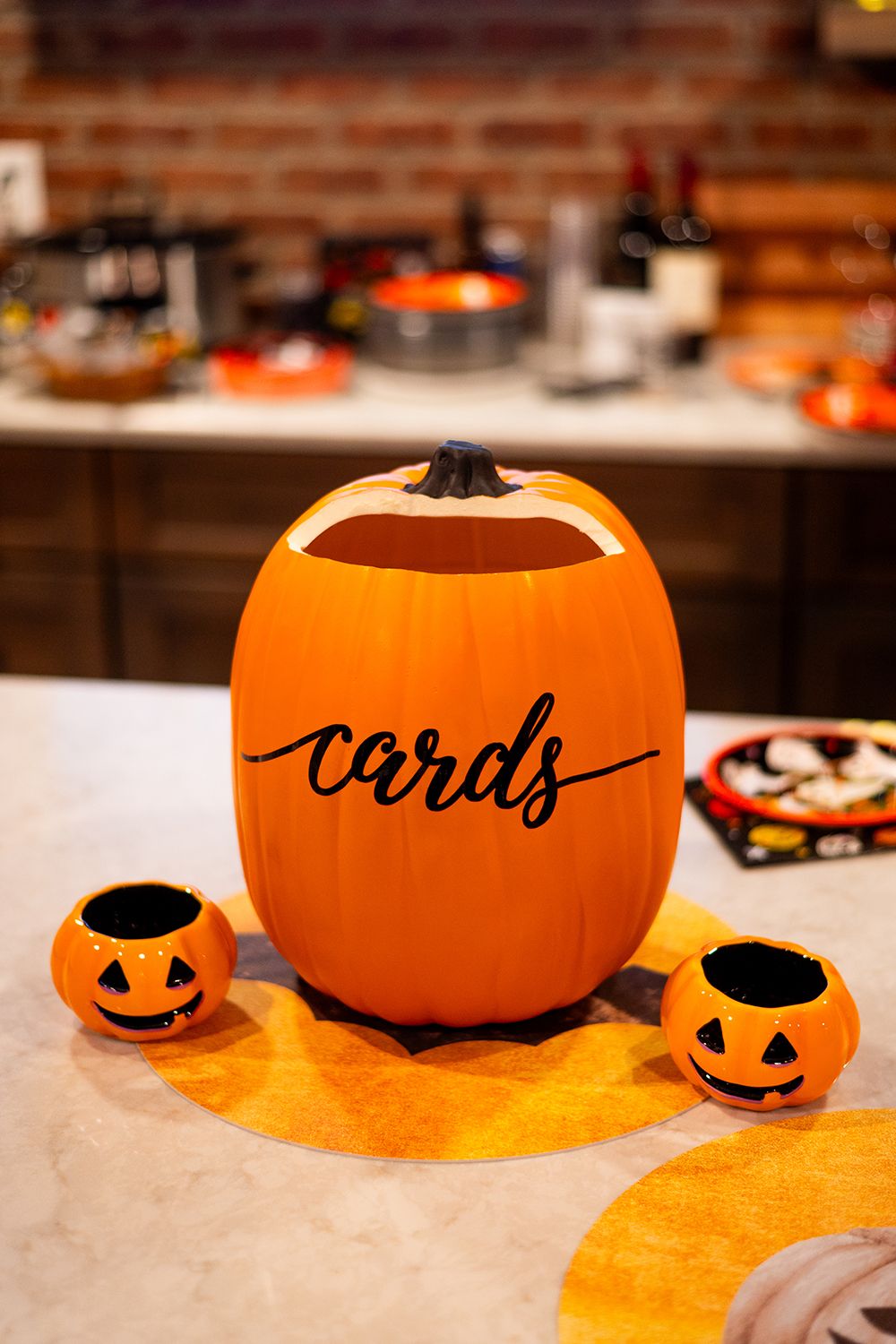 Halloween decorative orange 'cards' pumpkin with two small jack-o'-lantern votives displayed on a marble counter.