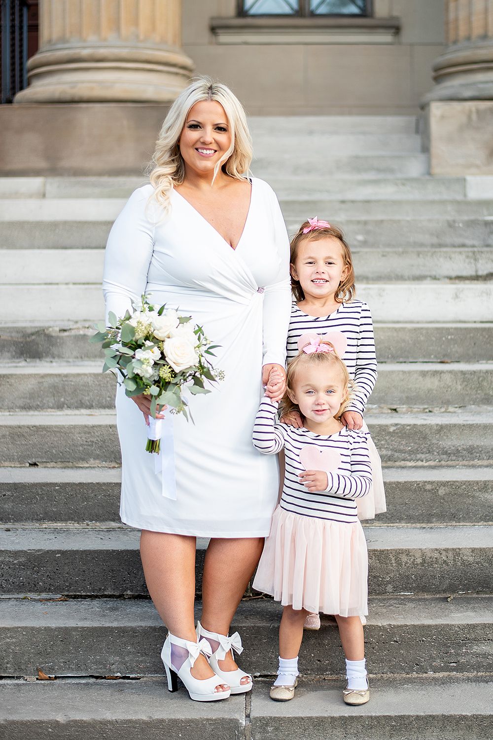 Two figures pose together on stone steps showing matching white and striped outfits with floral bouquets.