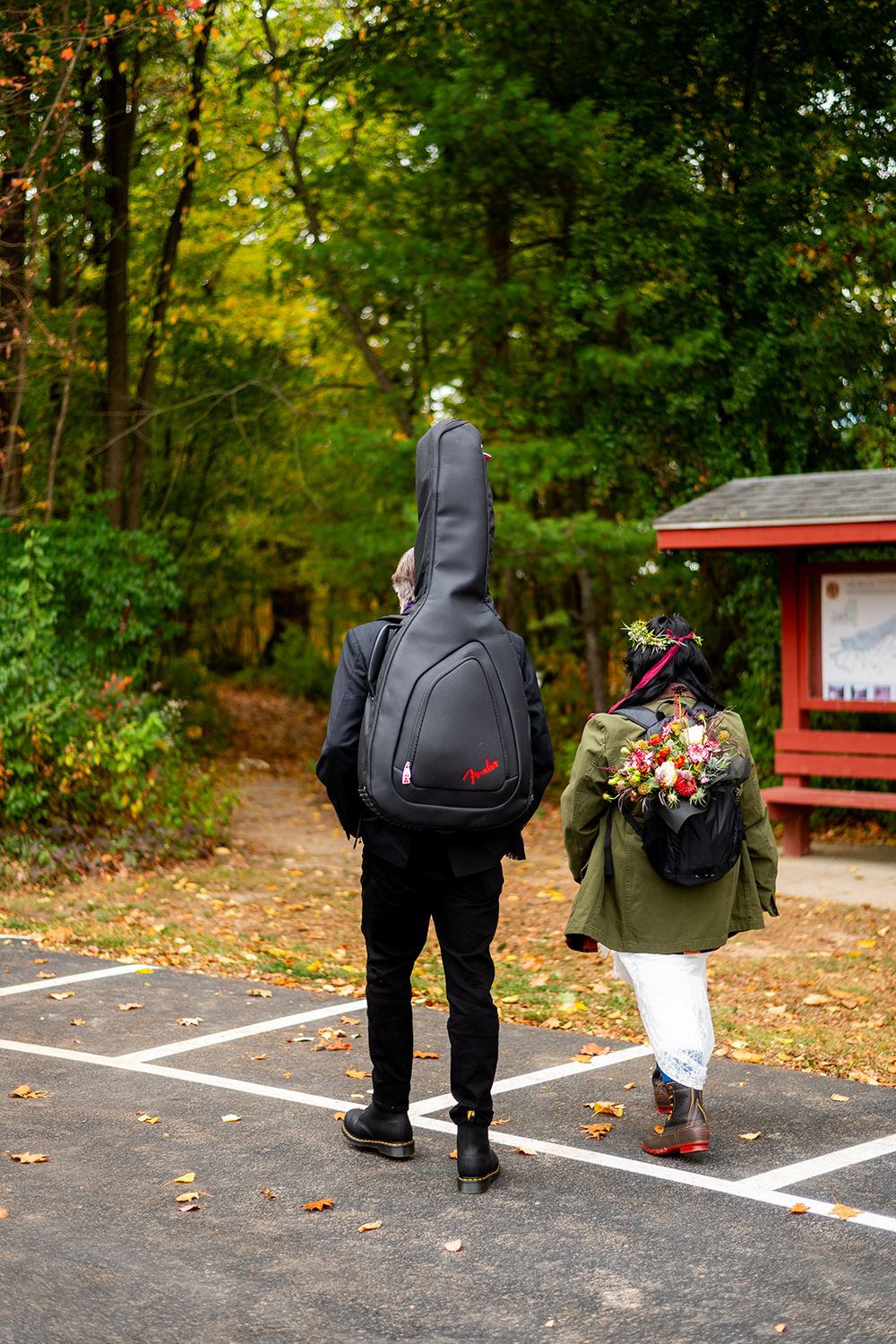 People walking through an autumn parking area with picnic tables and wooded surroundings.