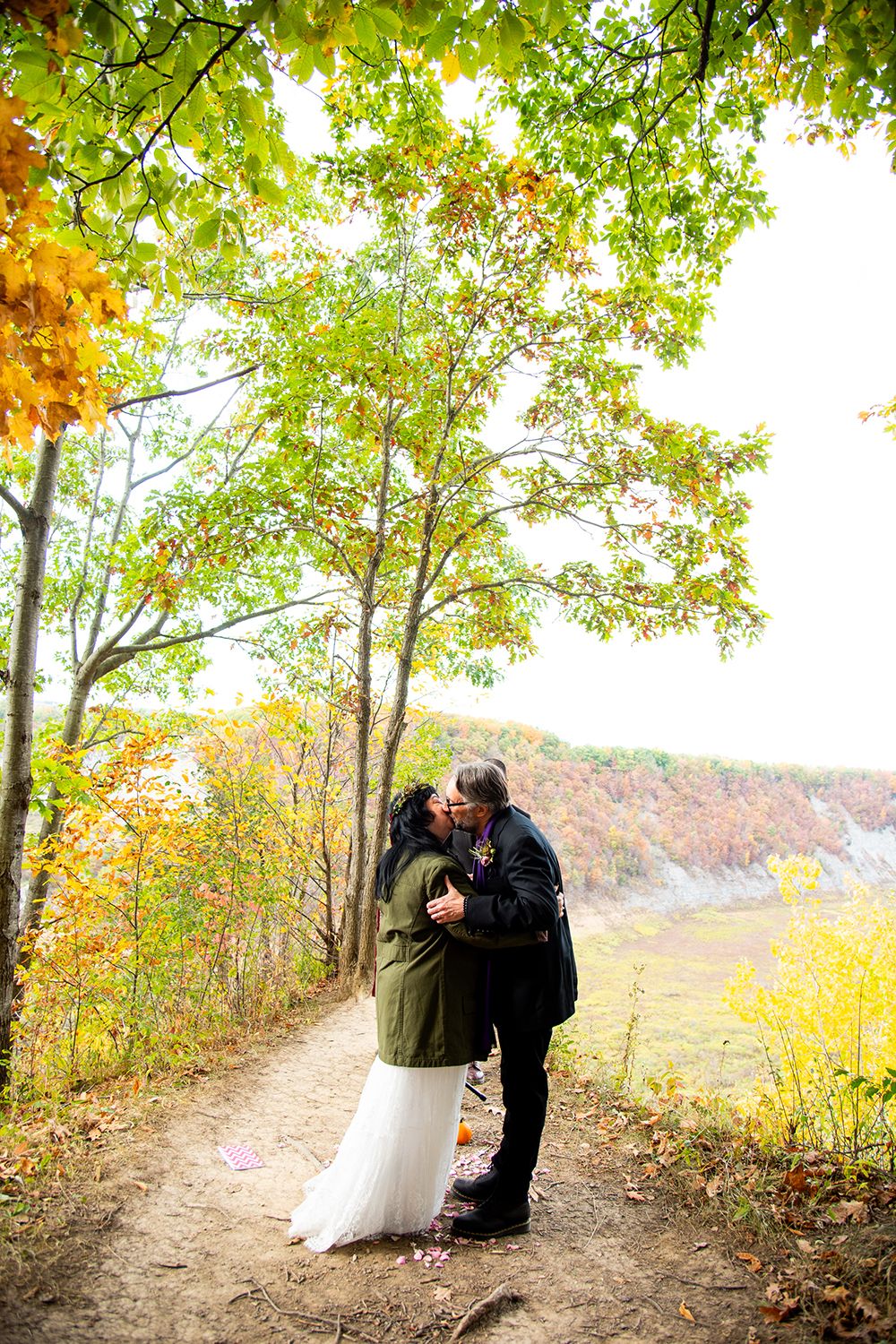 A romantic embrace on a forest trail with stunning fall foliage in the background.