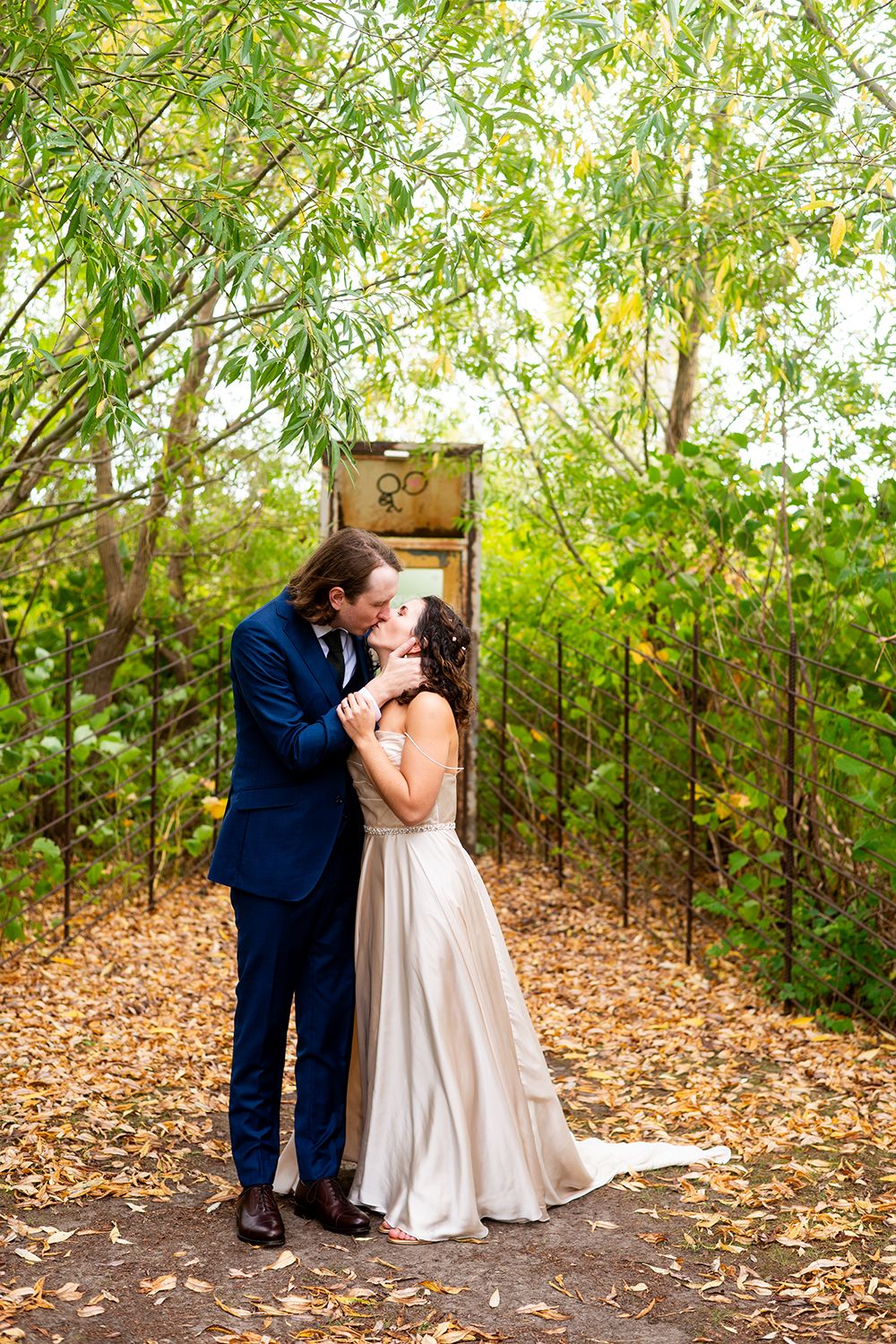 A romantic outdoor wedding photo showing a couple in formal attire standing in front of a rustic door framed by bamboo trees.