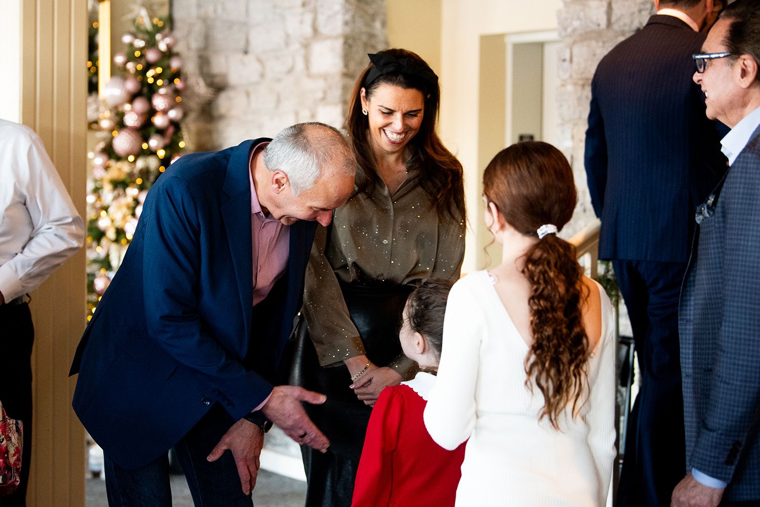 A joyful celebration scene with people gathered around a decorated Christmas tree in an elegant room.