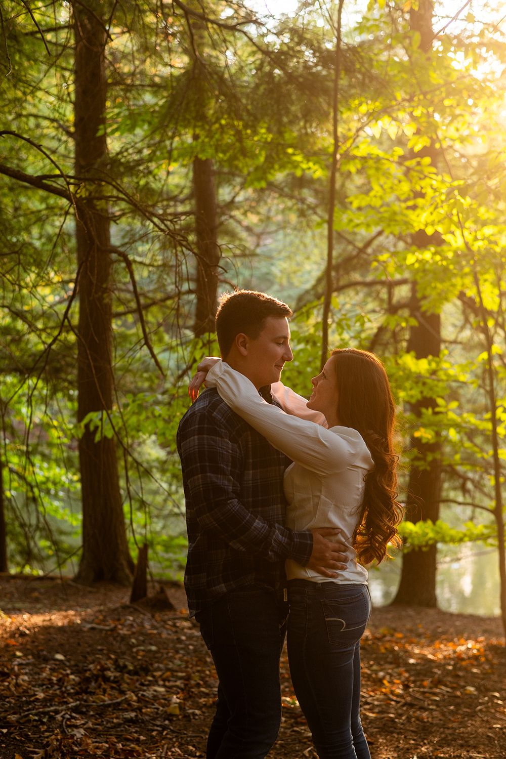 Silhouetted couple embraces in a sunlit autumn forest during golden hour.