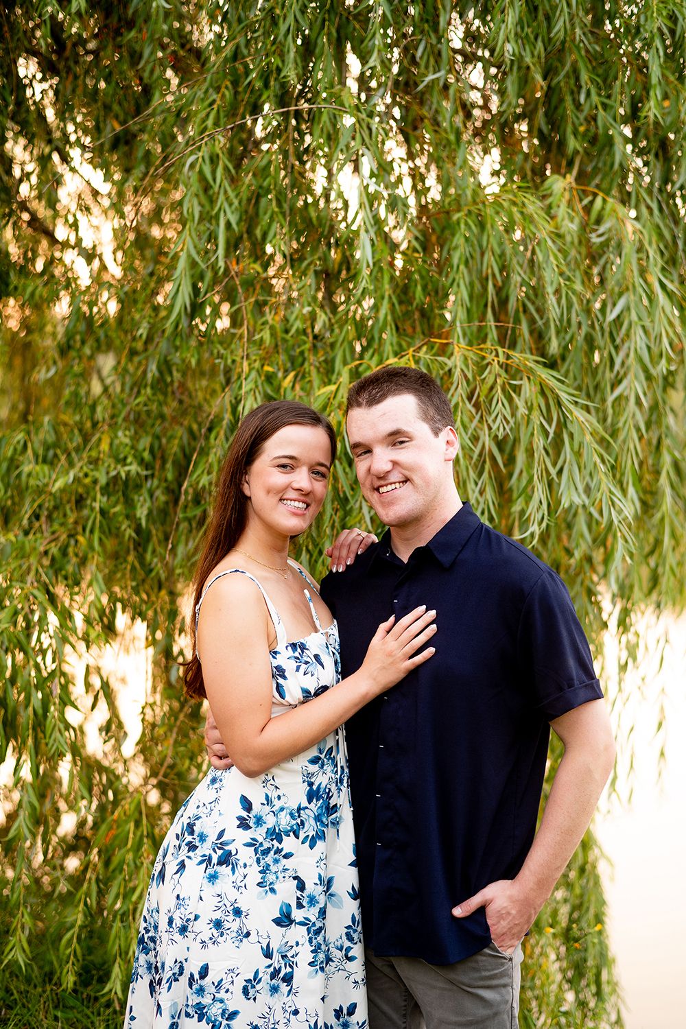 A couple shares loving moments together under weeping willow trees in a romantic outdoor photoshoot.