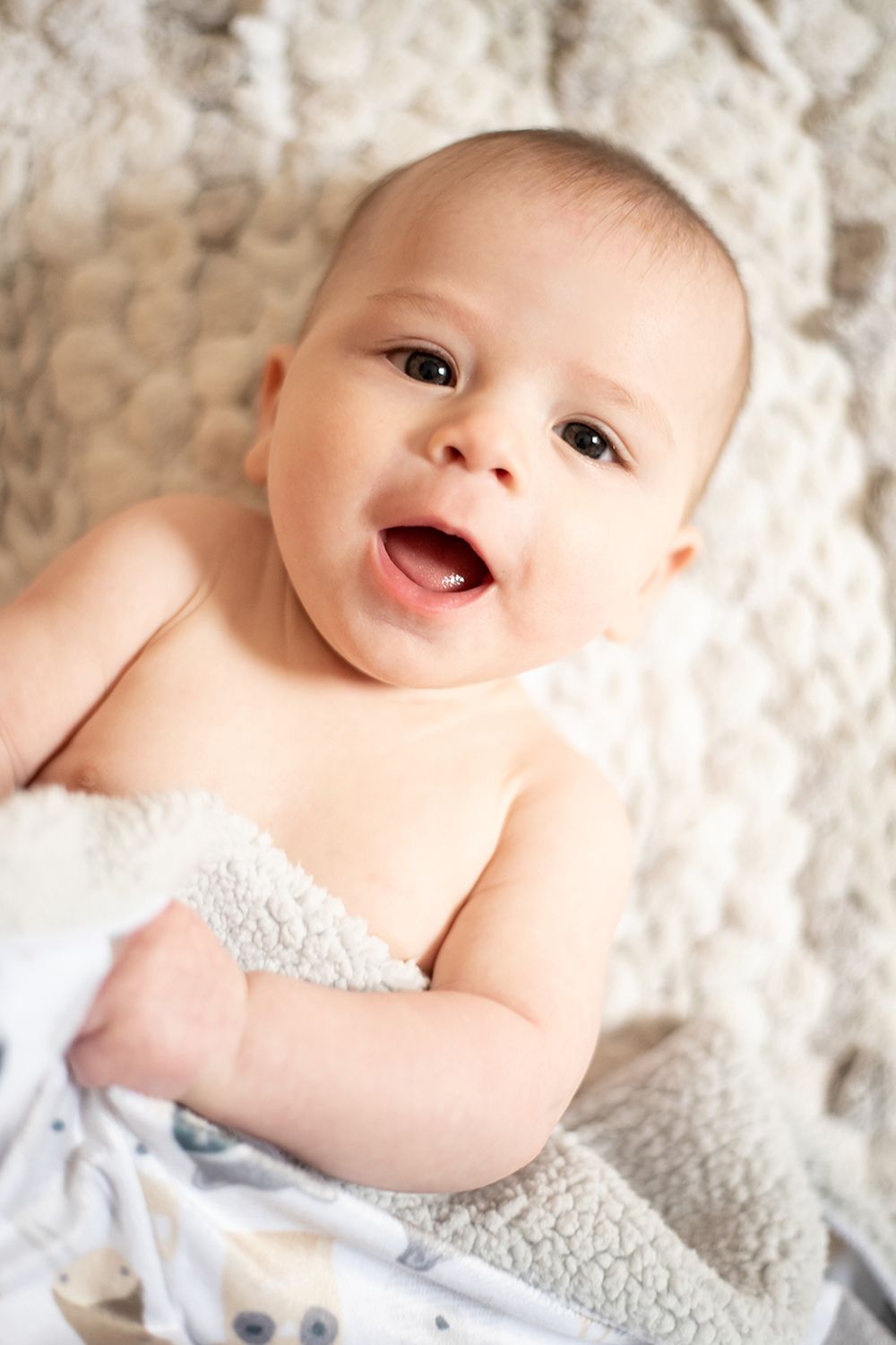 Happy baby lying on plush white blanket with a joyful expression during portrait session.