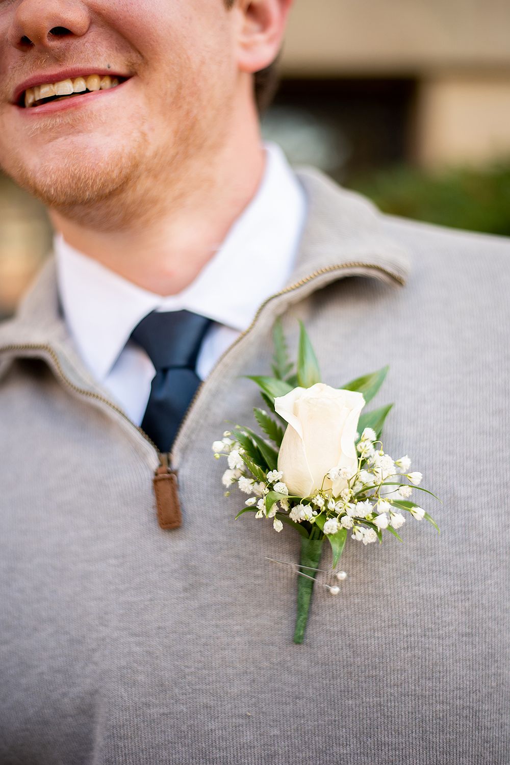 A row of buttonhole flowers featuring delicate white roses with baby's breath and greenery pinned on gray suit jackets.