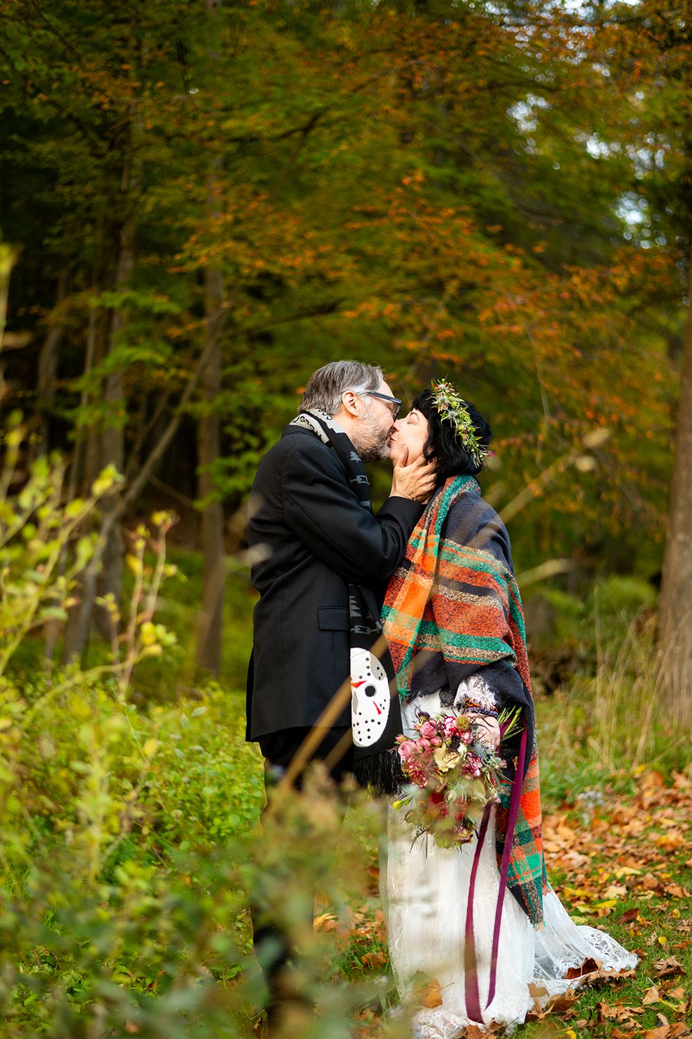 A tender kiss between newlyweds surrounded by golden fall foliage in a forest setting.
