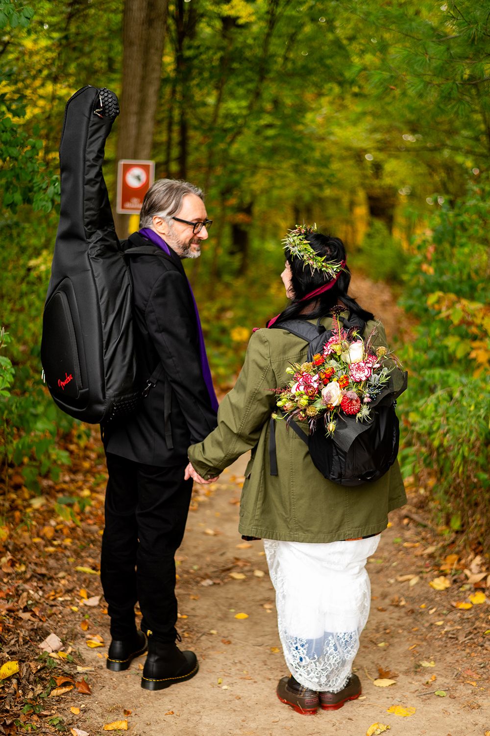A couple dances playfully on a wooded autumn path surrounded by golden foliage.