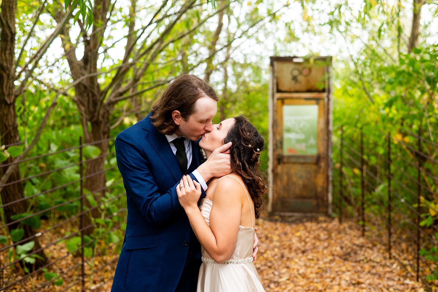 A tender moment between newlyweds sharing a kiss in front of an antique door surrounded by lush greenery.