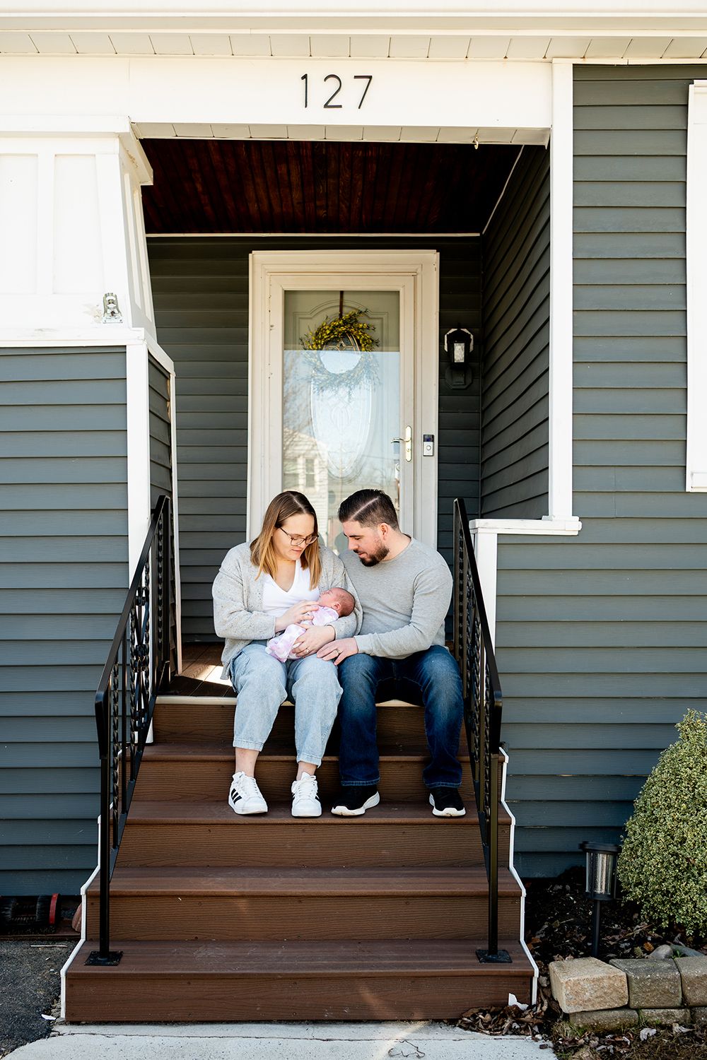 Family sits on front porch steps of gray house with white trim and house number 127.